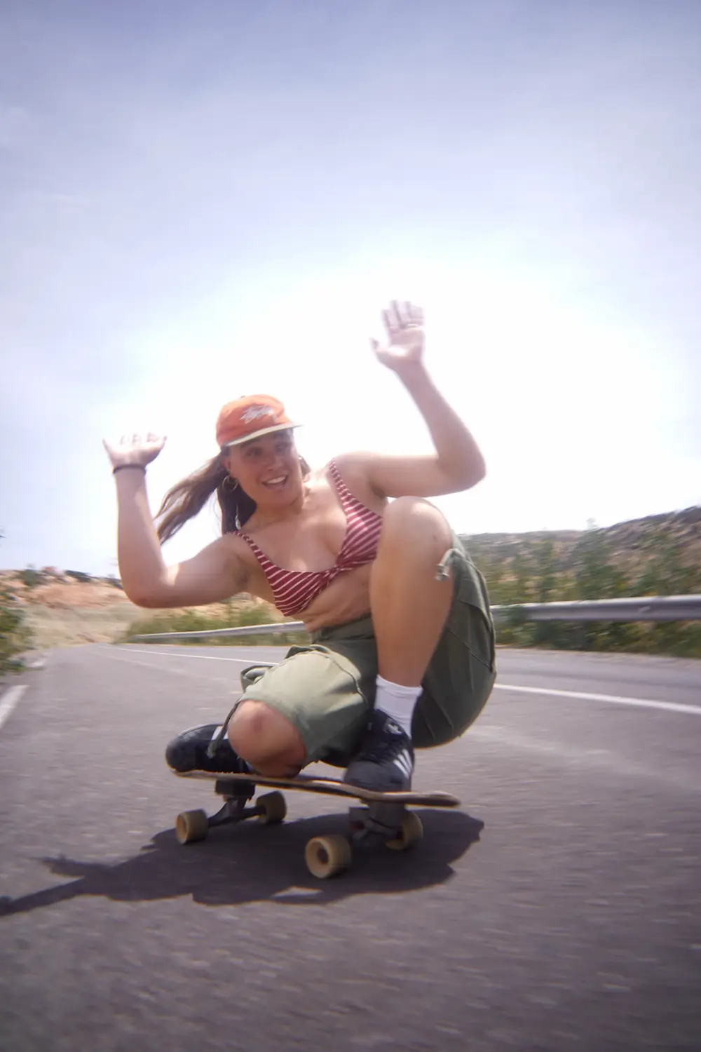 Crouch & Balance Guest in a red striped top crouching low on a surfskate on a coastal road in Imsouane, Morocco.